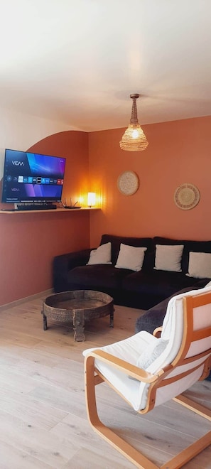 A living room with a flat-screen TV, a wooden coffee table, a sofa, a rocking chair, and a decorative wall hanging. - Samea Lodge • Beaches & Soulac • Quiet & Family-Friendly (Talais)