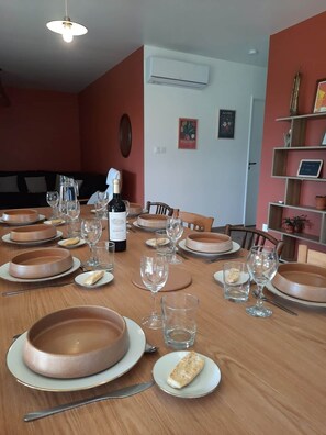 A dining room with a wooden table set for a meal, a bottle of wine, and a wall-mounted air conditioner. - Samea Lodge • Beaches & Soulac • Quiet & Family-Friendly (Talais)