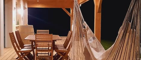 Une terrasse en bois avec une table et des chaises, ainsi que deux hamacs.