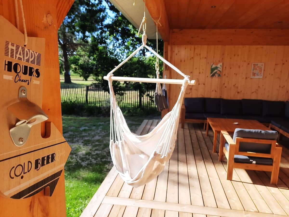A wooden deck with a hammock, outdoor seating, and a sign indicating cold beer availability.