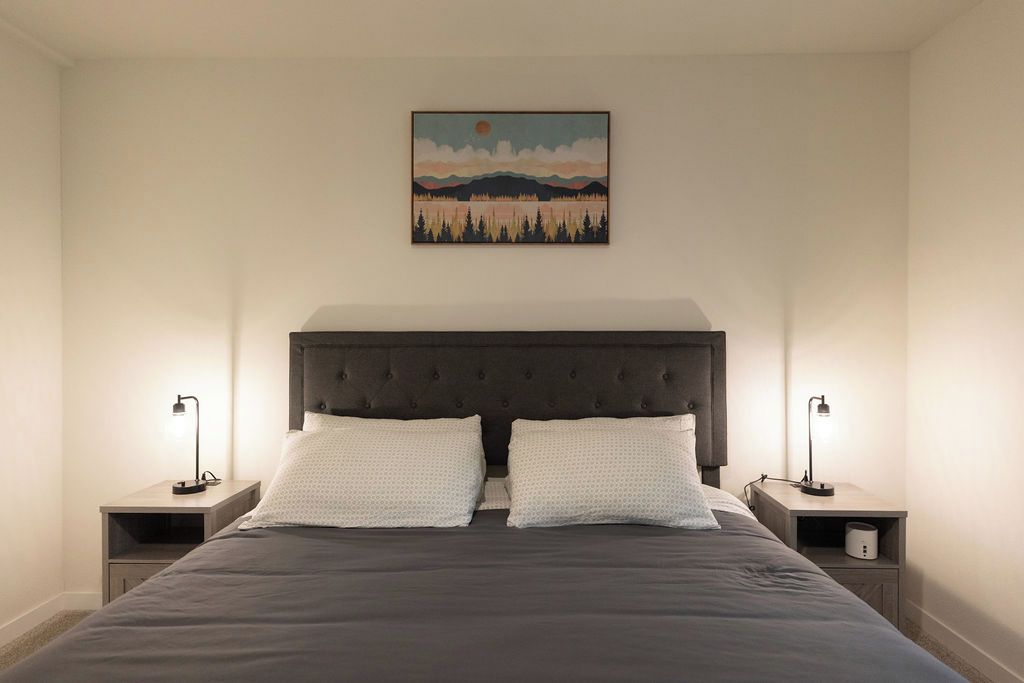 Une chambre à coucher avec un grand lit, deux tables de chevet et un tableau accroché au mur.