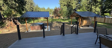 A wooden deck with a hot tub and covered seating area, surrounded by trees.