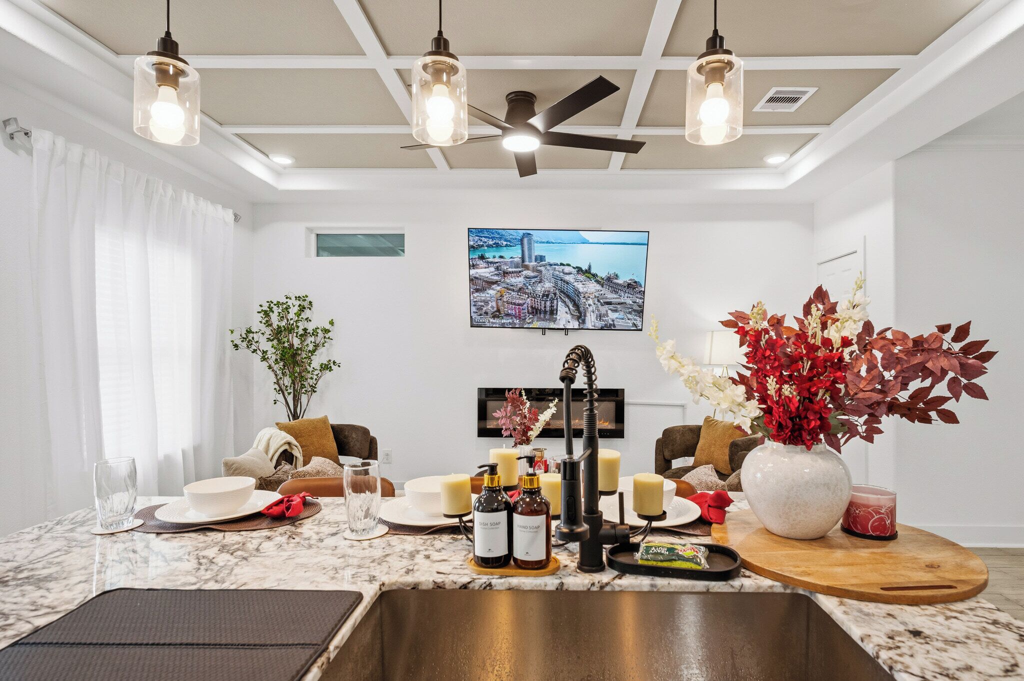 A modern hotel room with a marble countertop, a ceiling fan, a flat-screen TV, and a dining area set up with a vase of flowers and candles.