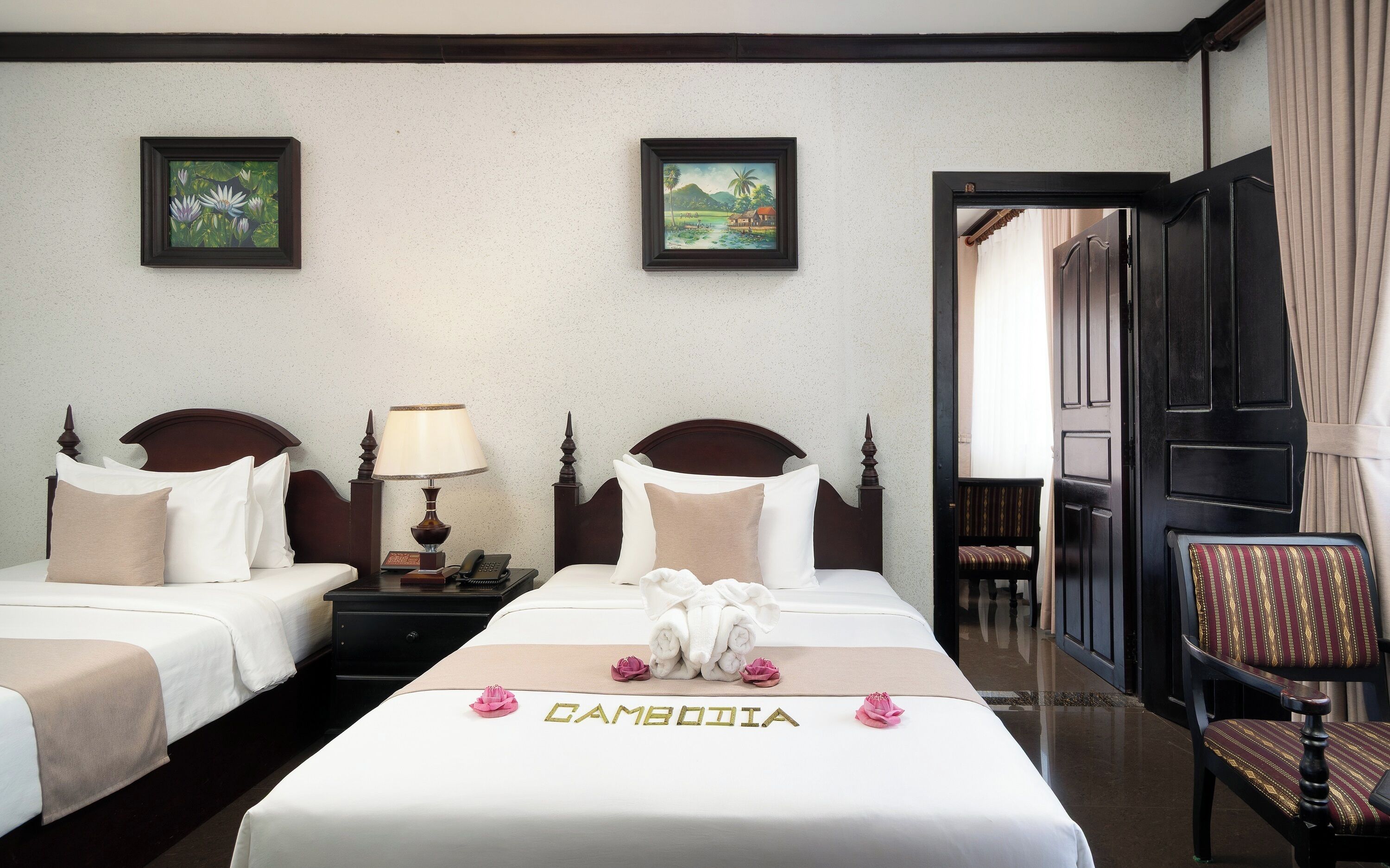 Une chambre d’hôtel avec deux lits, un bureau avec une lampe, une chaise et des œuvres d’art accrochées aux murs.