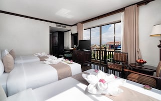 Habitación de hotel con dos camas, televisor, balcón con vistas y zona de comedor con mesa y sillas.