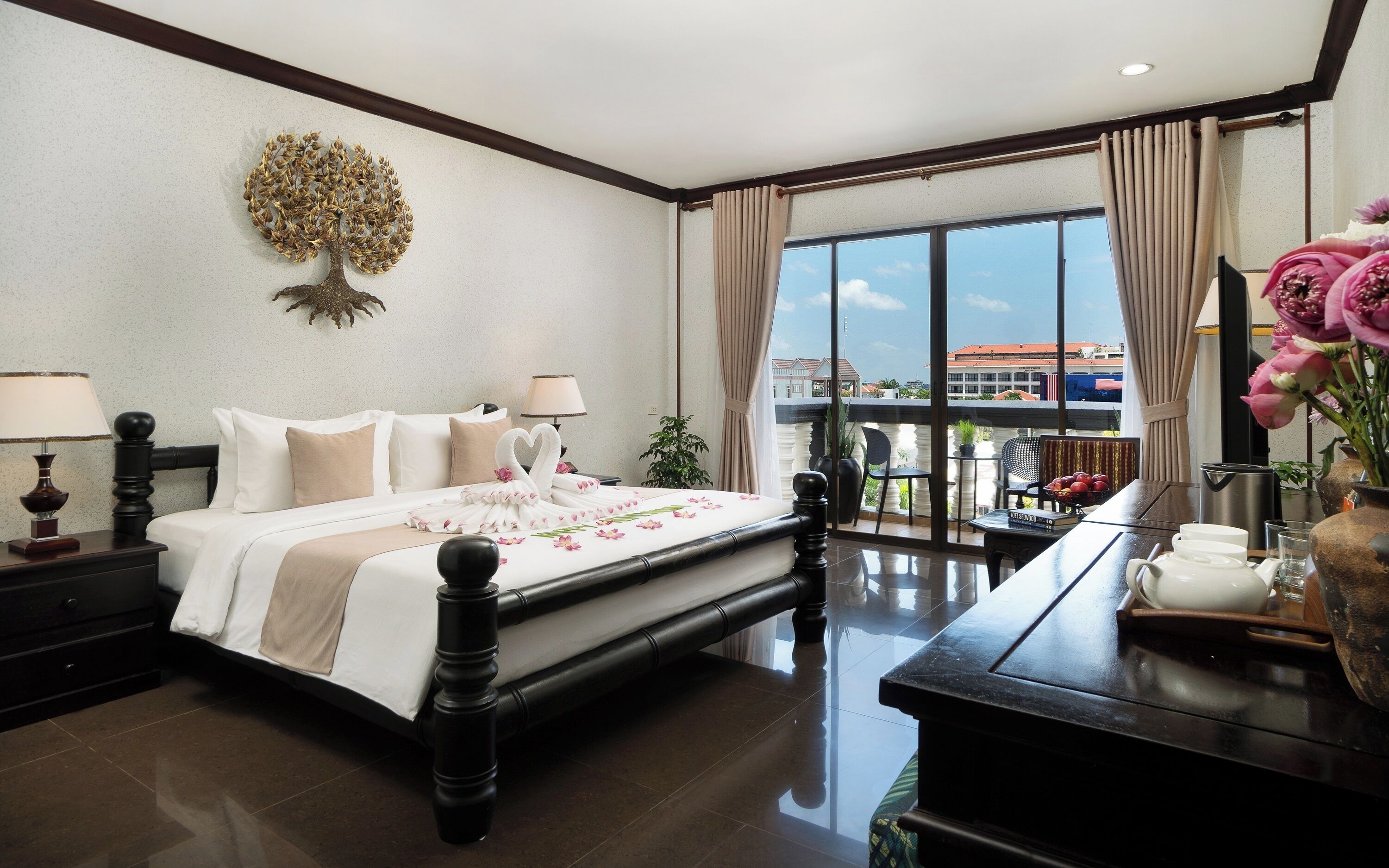 A hotel room with a large bed, a desk with a coffee maker, a view of the city, and a decorative tree on the wall.