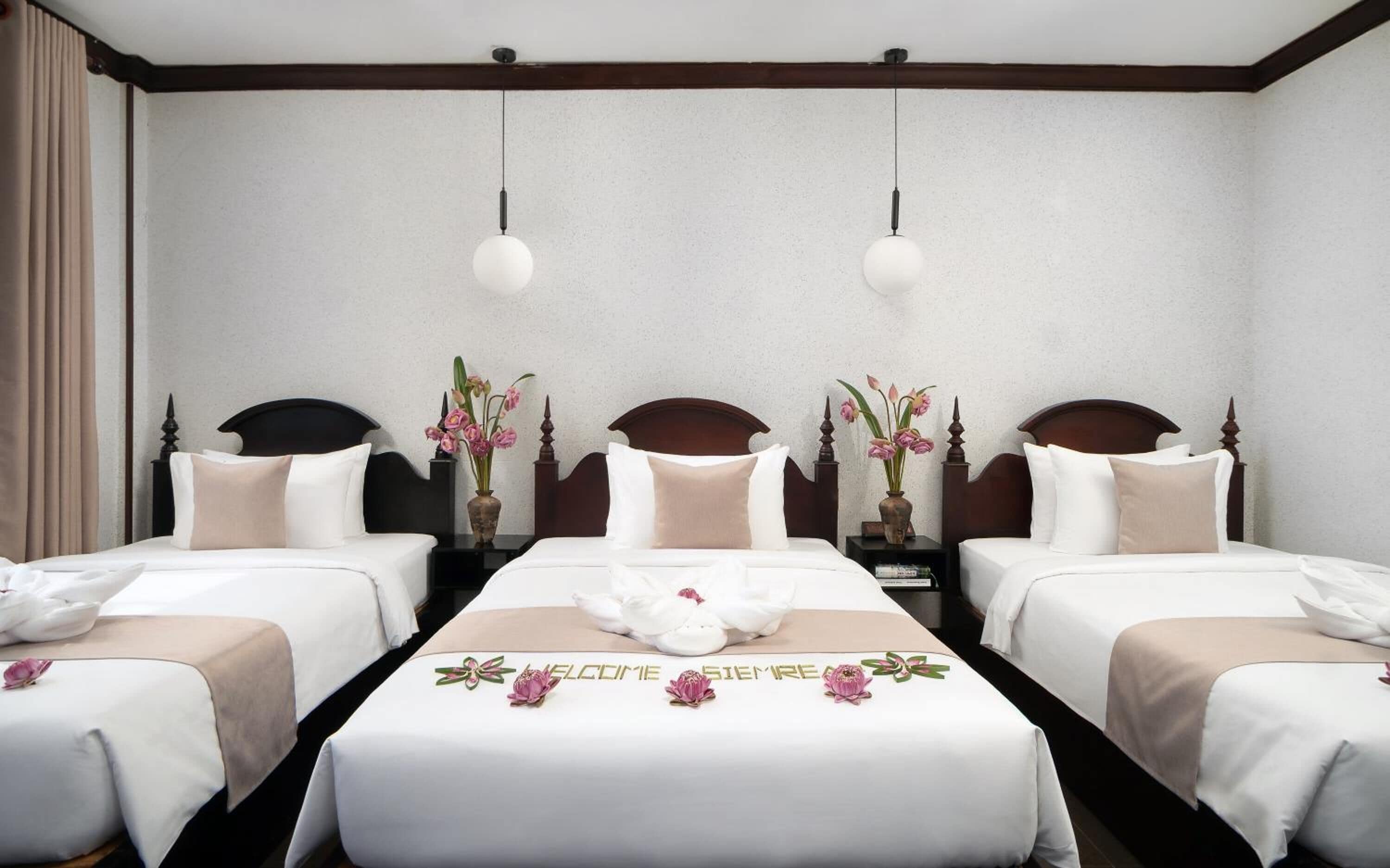 Una camera d'albergo con due letti, ognuno dotato di una testiera, comodini e un vaso con fiori.