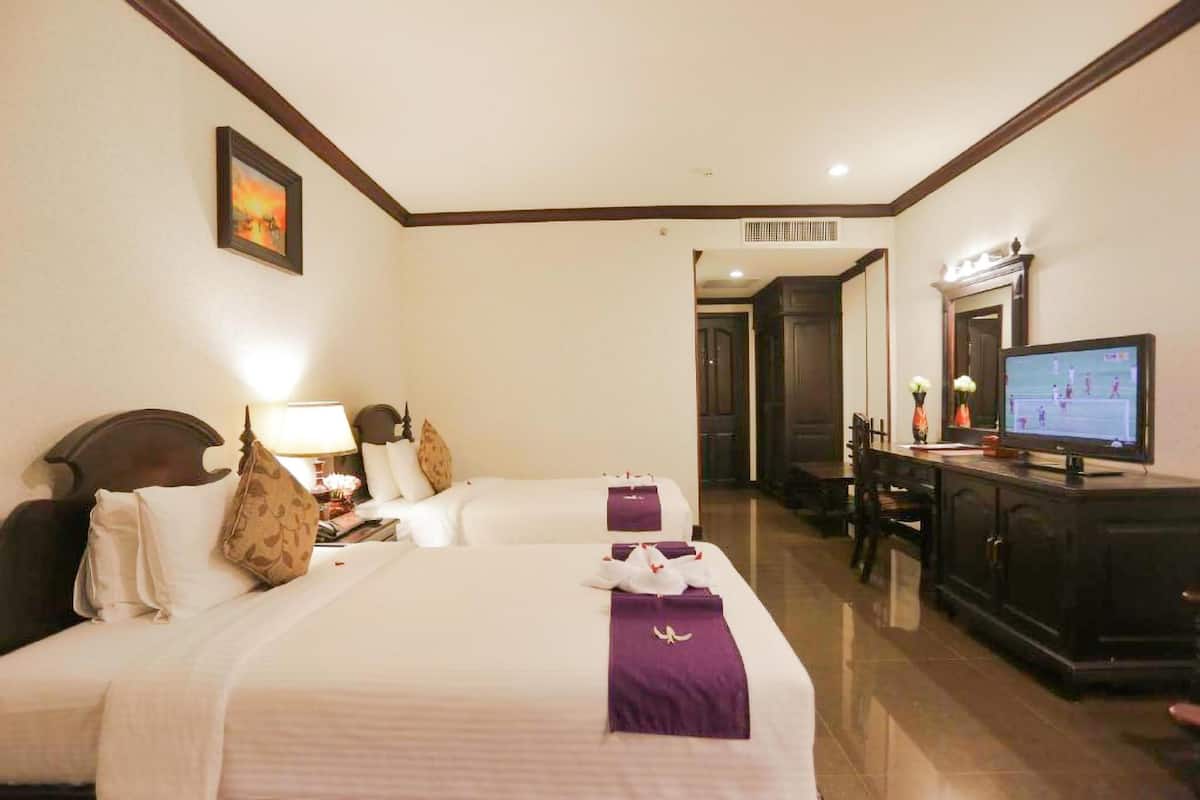 A hotel room with two beds, a TV, a desk, and a mirror.
