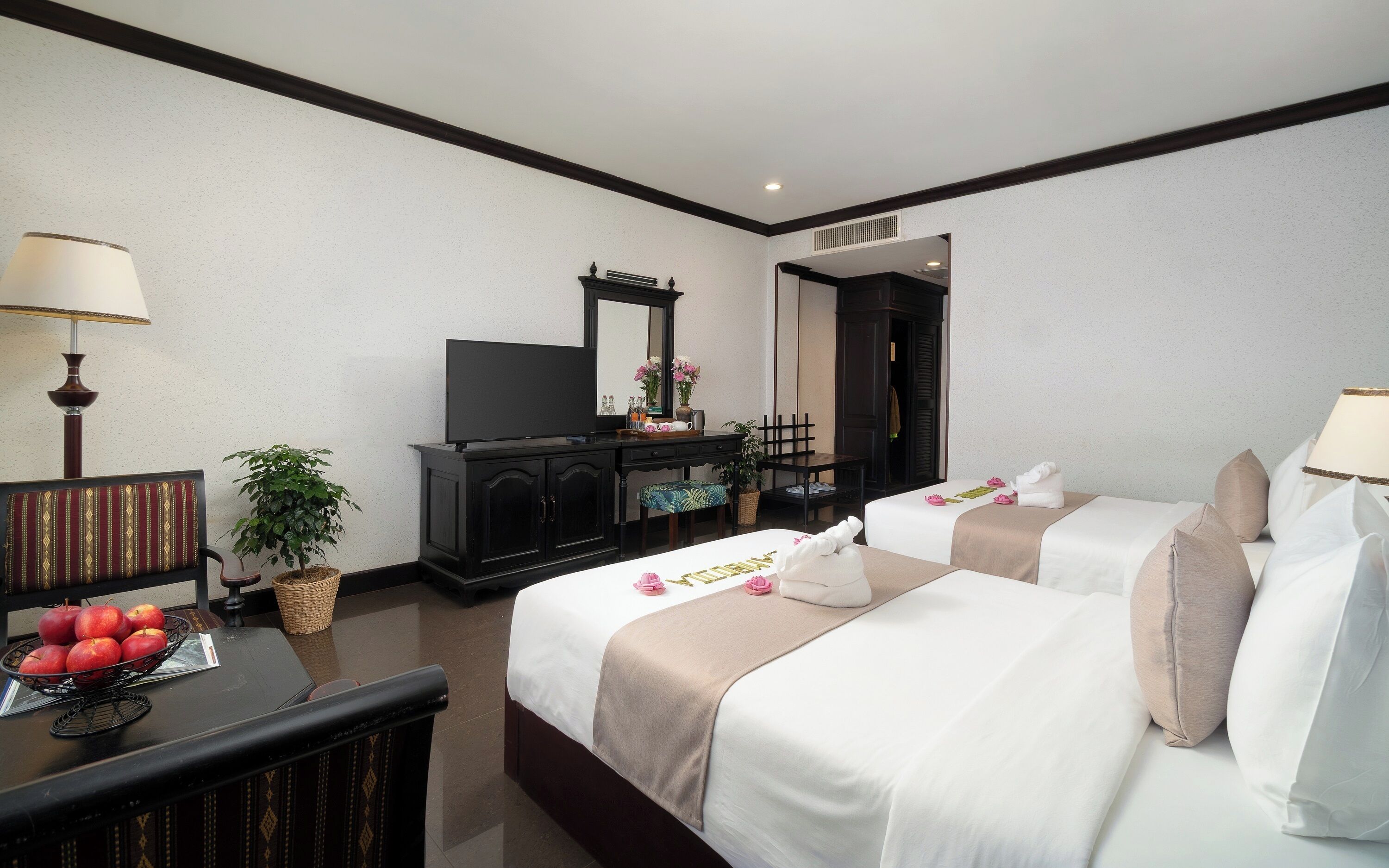 A hotel room with two beds, a desk with a lamp, a television, and a mirror.
