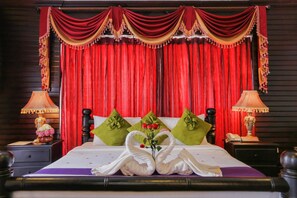 Una habitación de hotel con una cama, cortinas rojas, almohadas verdes y dos lámparas.
