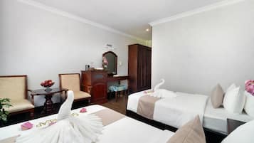 Une chambre d’hôtel avec deux lits, une commode en bois, une chaise, une petite table avec un panier de fruits et un miroir au mur.