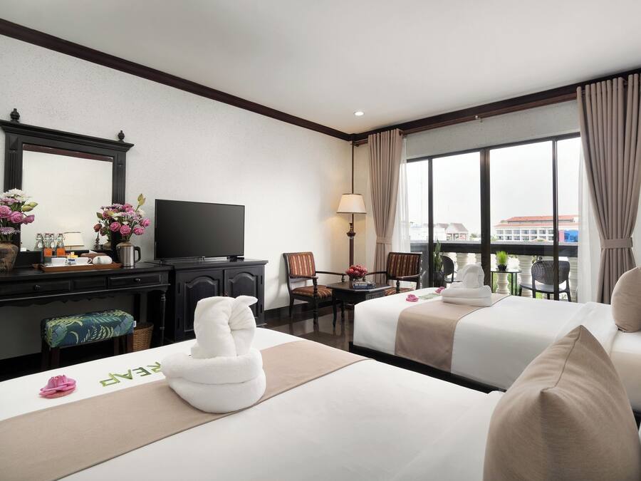 Habitació d'hotel amb dos llits, una televisió, escriptori amb làmpada i vista a la ciutat a través de grans finestres.