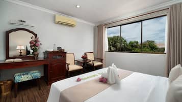 A hotel room with a bed, a desk, a chair, a mirror, and a window with a view of trees.