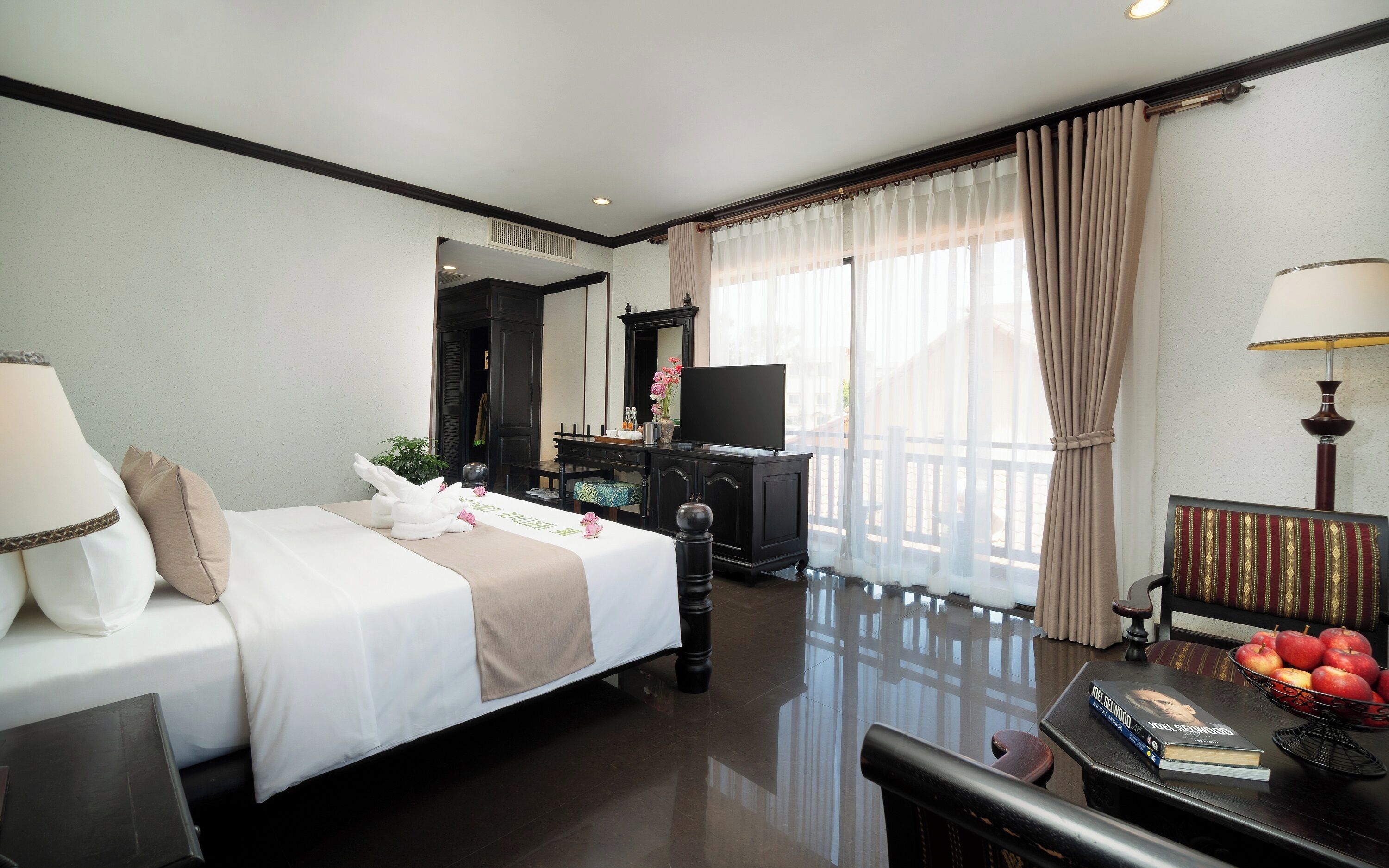 A hotel room with a bed, a TV, a desk with a lamp, a chair, and a window with curtains.