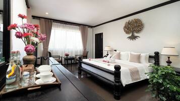 Une chambre d’hôtel avec un lit, des lampes de chevet, une table avec un plateau de verres et un vase de fleurs, une chaise, un bureau et une fenêtre avec des rideaux.