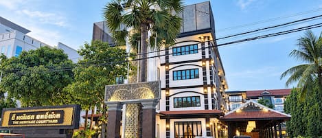 Un hotel de varios pisos con una entrada destacada, palmeras y un letrero que dice 'The Heritage Courtyard'.