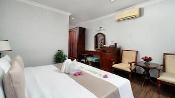 A hotel room with a bed, a desk, a chair, a small table with fruit, and an air conditioning unit.