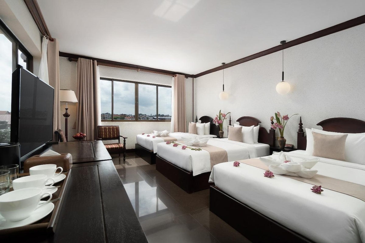 A hotel room with two beds, a TV, a dining table with cups, and a view of the city.