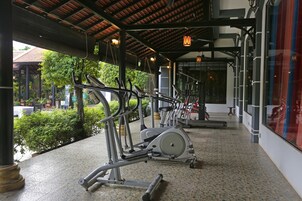 Zona de gimnasio al aire libre techada con equipo de ejercicio, piso de baldosas y vistas a la vegetación.