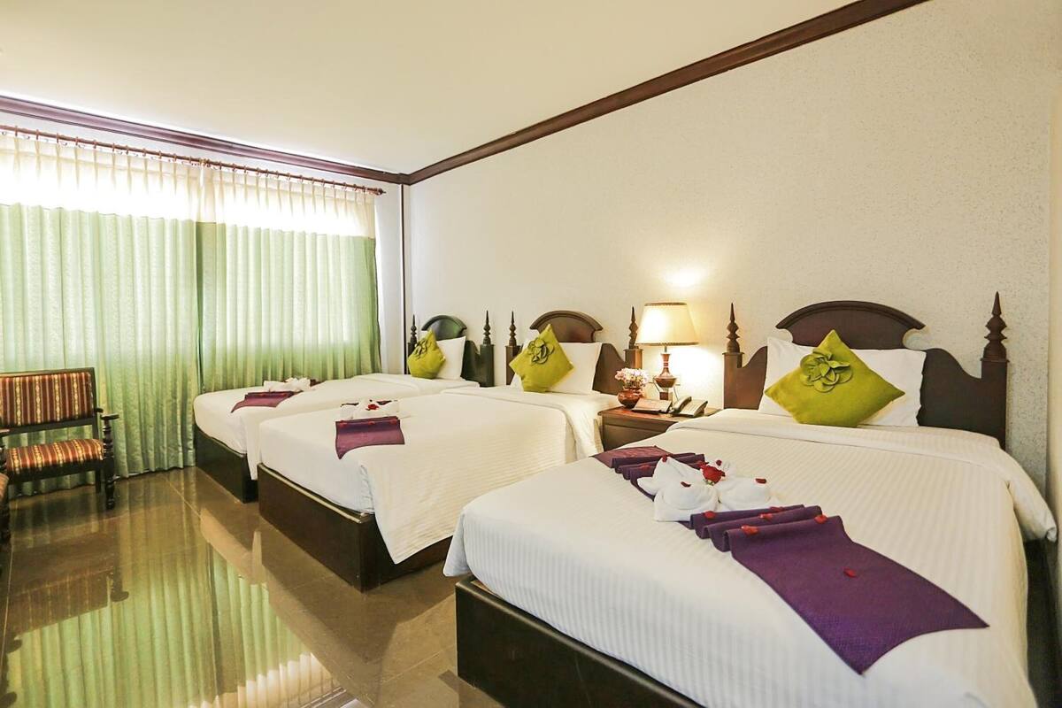 Habitació d'hotel amb tres llits, una zona de seients amb una cadira i un gran finestral amb cortines.