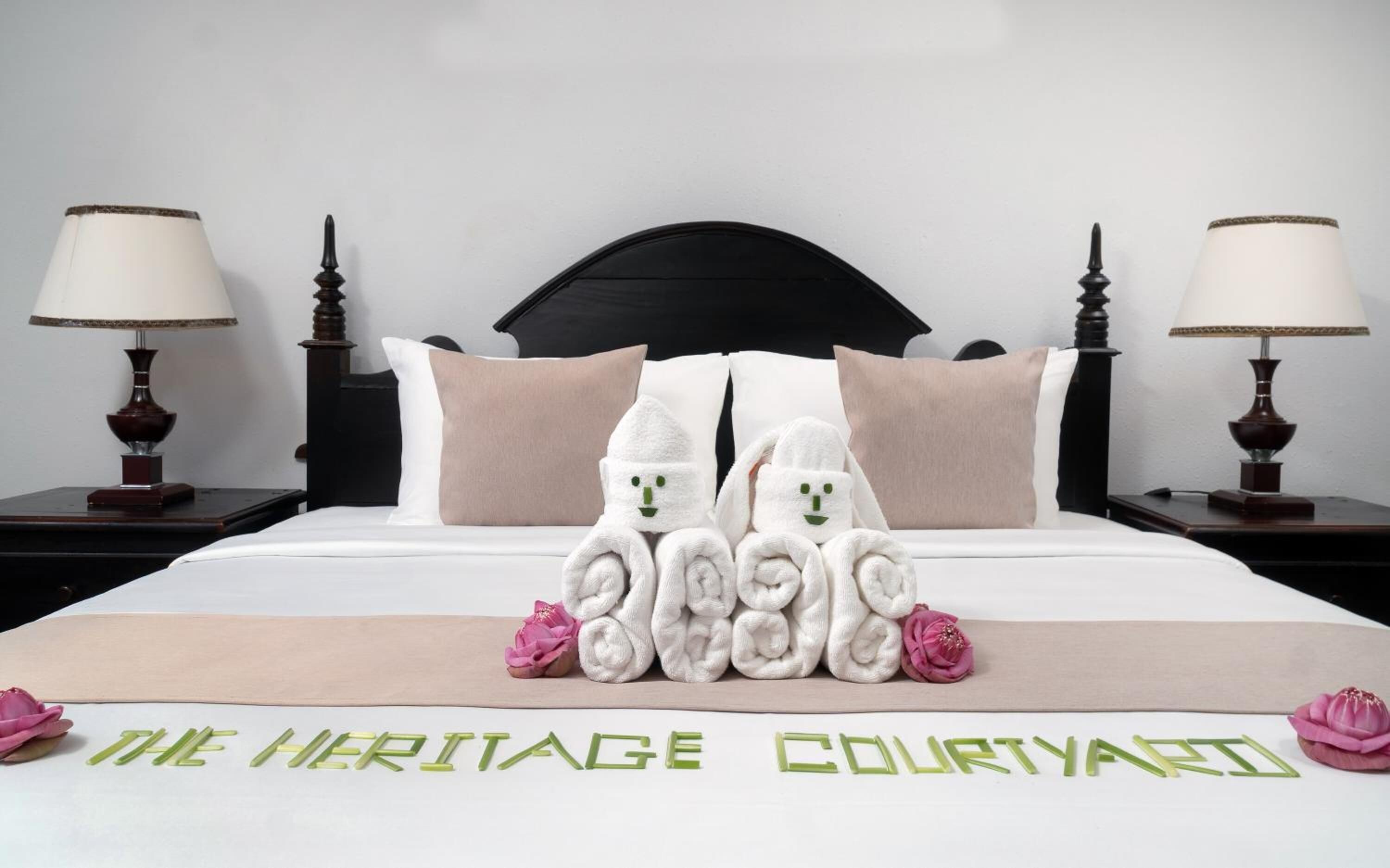 Habitación de hotel con cama, dos mesitas de noche, cabecero y una decoración de toallas sobre la cama.
