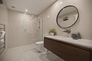 Ein modernes Badezimmer mit einer Duschkabine, einer weißen Toilette, einem Waschtisch mit Spiegel und einer Topfpflanze.