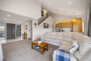 A modern living room with a large L-shaped sofa, a wooden coffee table, and a staircase leading to an upper level. - Middleton Vista - Perfect lake and mountain views. Great for families and groups (Queenstown)
