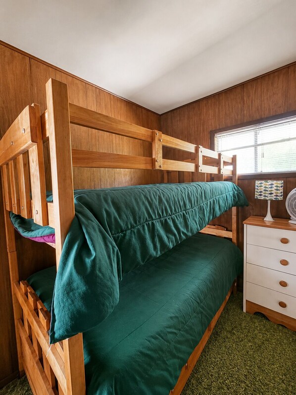 Una cama litera con colchón verde, cabecera de madera y una mesita de noche blanca con cajones.