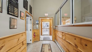 A hallway with wooden paneling, framed certificates on the walls, an exit sign, and a hand sanitizer station. - Uncas by Avantstay Sleeps 7 + Bunk Room + 3 Baths Resort Pool + Game Room Gore Mountain (North Creek)