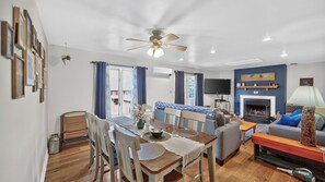 A well-lit living room with a fireplace, a dining area with a table and chairs, and a seating area with a sofa and armchairs. - Uncas by Avantstay Sleeps 7 + Bunk Room + 3 Baths Resort Pool + Game Room Gore Mountain (North Creek)