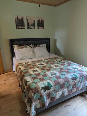 A bed with a quilt, a headboard, and three wall-mounted pictures. - Peaceful Cabin on Reed Lake near Haywar, WI (Hayward)