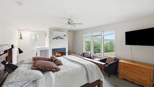Ein Schlafzimmer mit Bett, Kamin, Fernseher, Schreibtisch und Blick ins Freie.