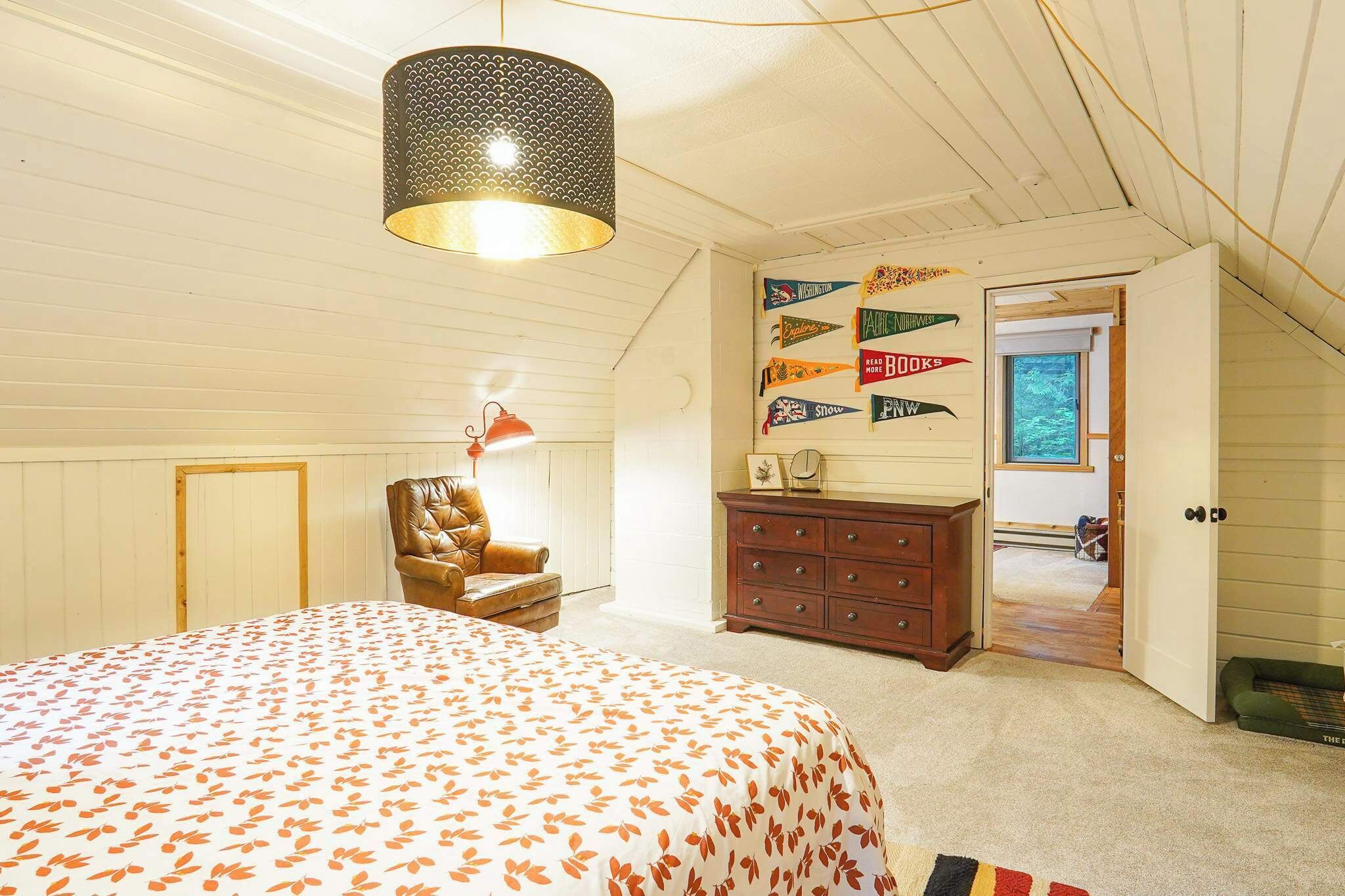 A bedroom with a bed, a chair, a dresser, a hanging lamp, and a wall with directional signs.