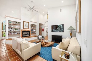 Ein modernes Wohnzimmer mit Kamin, weißen Sofas, einem Glastisch und einem blauen Teppich.