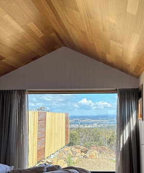 A room with a large window, wooden ceiling, and a view of a landscape.