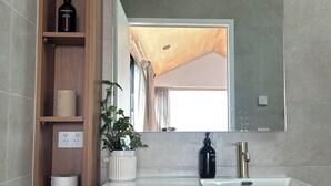 A bathroom with a wooden shelf, a potted plant, a sink, and a large mirror.