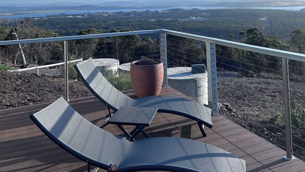 A deck with lounge chairs and a large planter, overlooking a scenic landscape with distant hills and a body of water.
