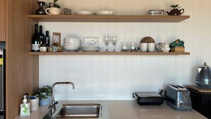 A kitchen with wooden shelves holding various items, a stainless steel sink, and a toaster.