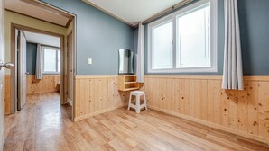 Een kamer met houten lambrisering, een houten vloer, een witte kruk en een raam met gordijnen.