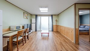 Een kamer met een houten vloer, een eettafel met stoelen, een magnetron, een televisie, een koelkast en een bed met hoofdeinde.