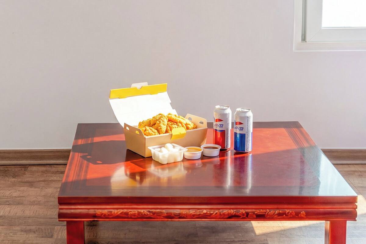 Una mesa con un cubo de pollo frito, dos latas de refresco y recipientes pequeños de salsas.