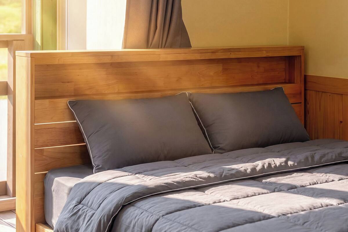Una cama con cabecera de madera, ropa de cama gris y una ventana con cortinas.
