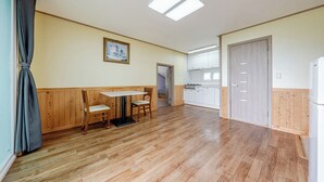 Een kamer met houten vloer, een eettafel met stoelen, een keukenhoek en een deur die naar een andere kamer leidt.