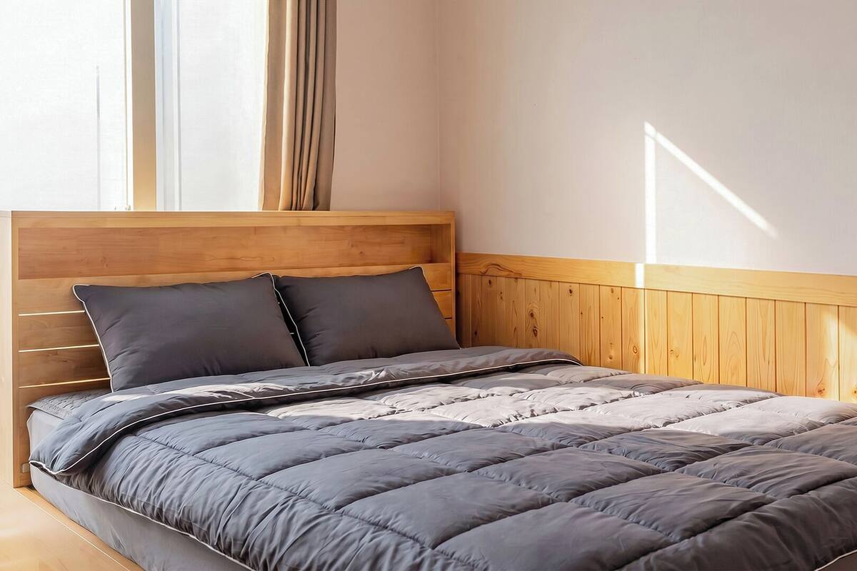 Una cama con cabecera de madera, ropa de cama gris y una ventana con cortinas.
