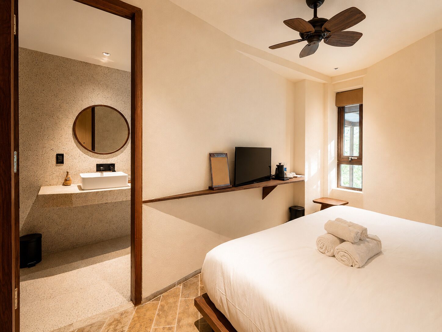 A hotel room with a bed, a television, a bathroom with a sink and mirror, and a ceiling fan.
