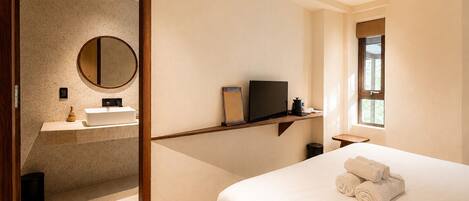 A hotel room with a bed, a television, a bathroom with a sink and mirror, and a ceiling fan.