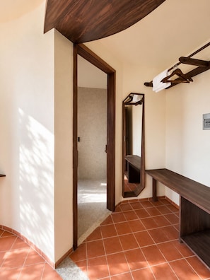 Um corredor com um banco de madeira, um espelho e uma porta que dá para outro quarto.