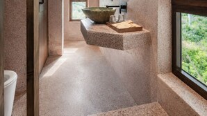 Un baño moderno con un lavabo de piedra grande, un espejo redondo y vistas a zonas verdes.