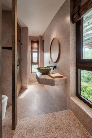 Un baño moderno con un lavabo de piedra grande, un espejo redondo y vistas a zonas verdes.