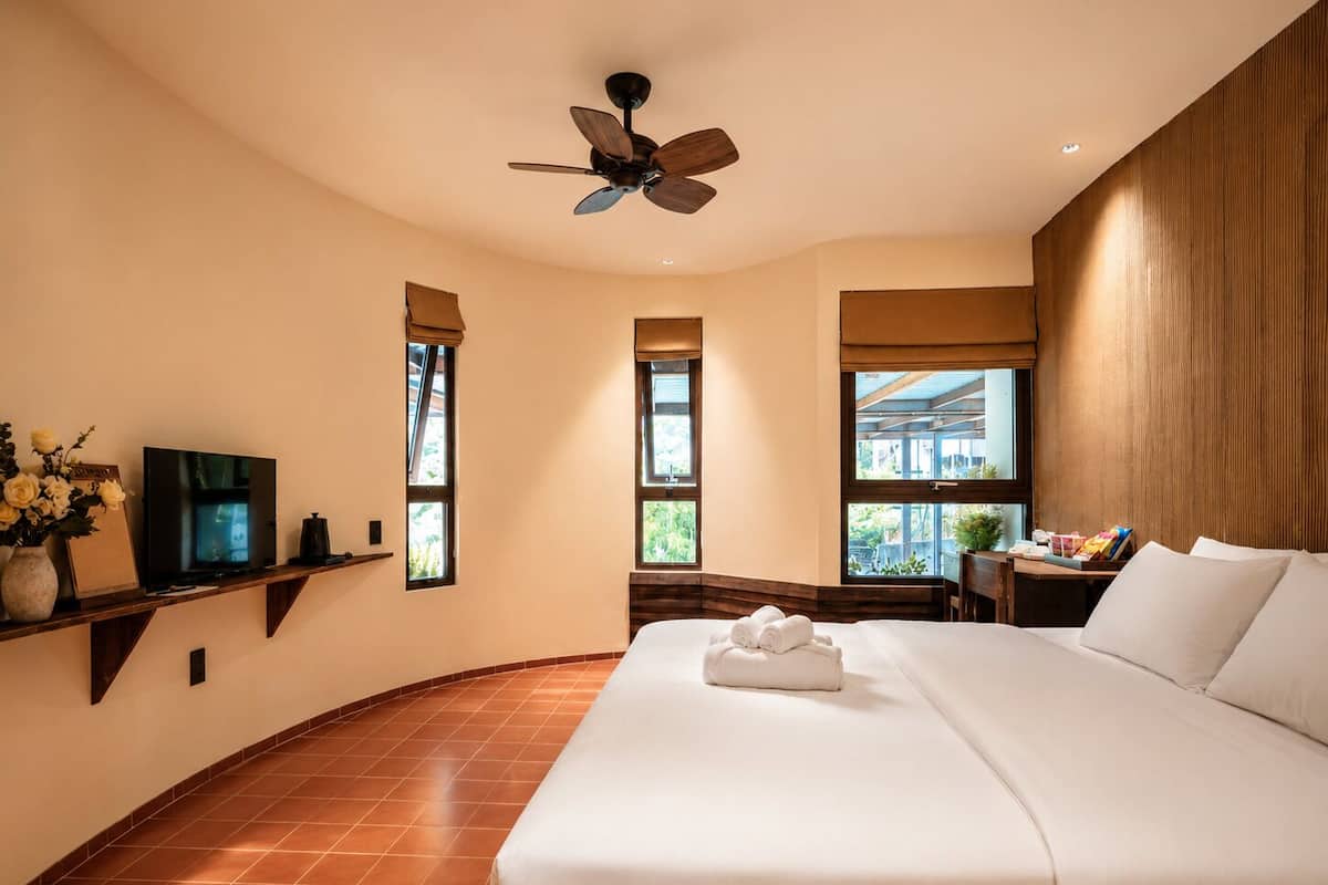 A hotel room with a bed, a ceiling fan, a TV, and windows with views.